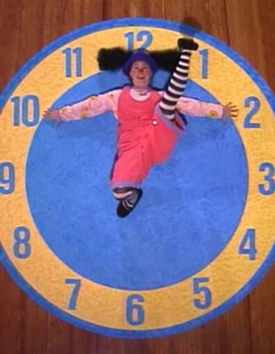 Loonette from The Big Comfy Couch on a floor rug shaped like a clock, her leg up by the one and arms splayed