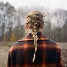 Album cover for evermore by Taylor Swift.

Taylor Swift stands with her back to us in a plaid, brown, orange and black coat with her blonde hair in a braided ponytail. Looking at trees with few leaves in front of her, facing us.