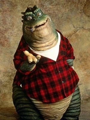 Auf dem Bild ist die Figur Earl Sinclair aus der TV-Show die Dinos mit einer Zigarre im Mund und ausgestreckten Arm zu sehen.