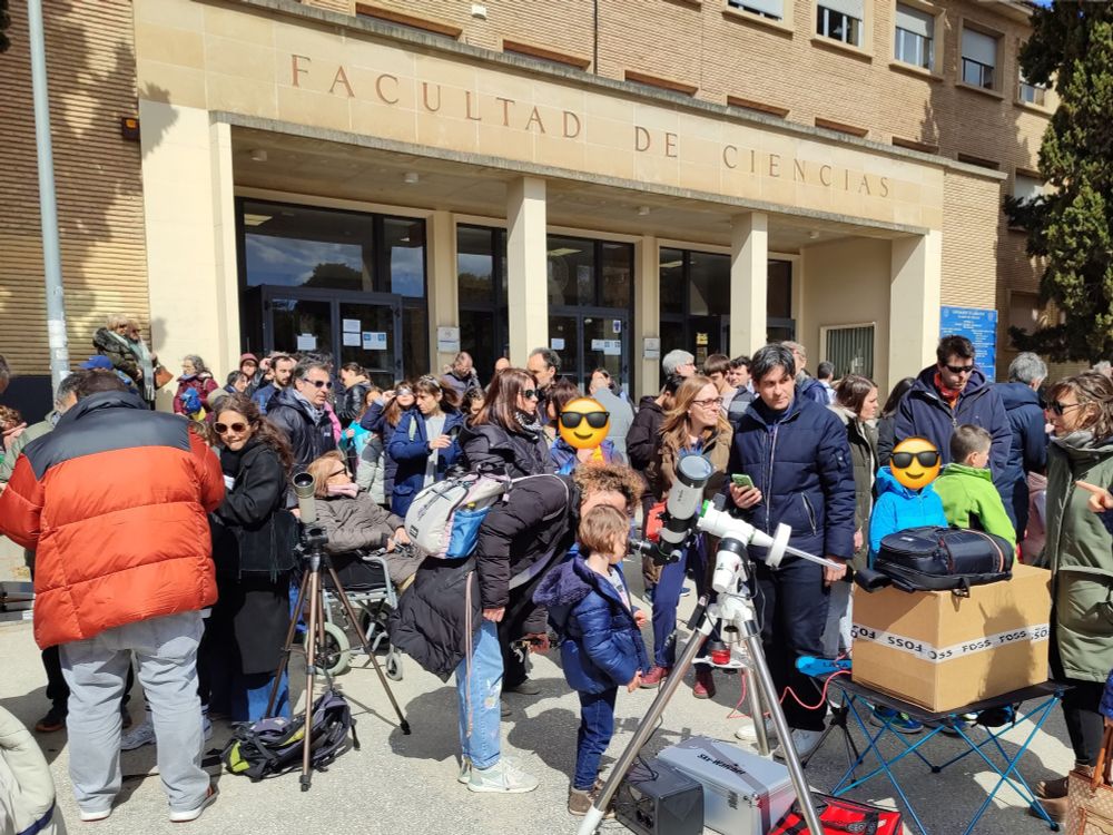 Decenas de personas de todas las edades reunidas frente al edificio de física de la Facultad de Ciencias.
Se ven algunos telescopios de la Agrupación Astronómica Aragonesa por los que la gente contempla el eclipse de Sol.