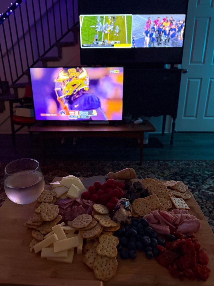 charcuterie board on a lap table with white whine in front of multiple tvs playing college football 