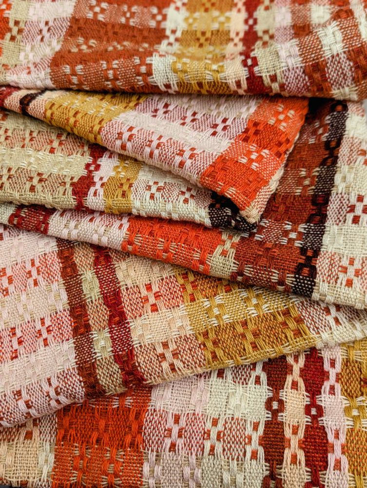 Textured scarf woven in intersecting bands of orange, pink, yellow, burgundy, beige,  and cream. Fabric is casually folded.