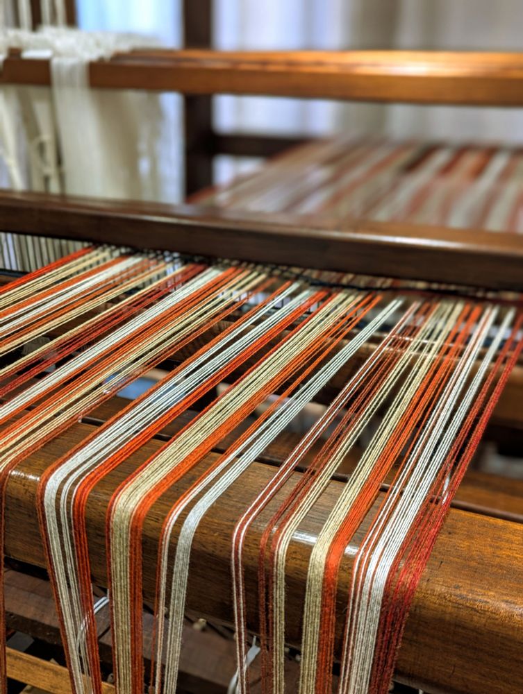 Merino warp in shades of white, cream, burnt orange, rust, terracotta, bright orange being wound onto a wooden floor loom