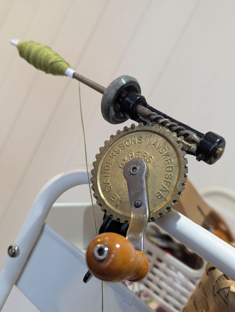 Metal bobbin winder, winding lime green 8/2 cotton thread. Winder has a wooden handle. 