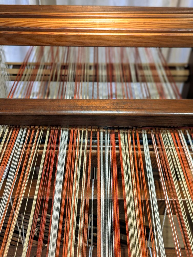 Merino warp in shades of white, cream, burnt orange, rust, terracotta, bright orange being wound onto a wooden floor loom