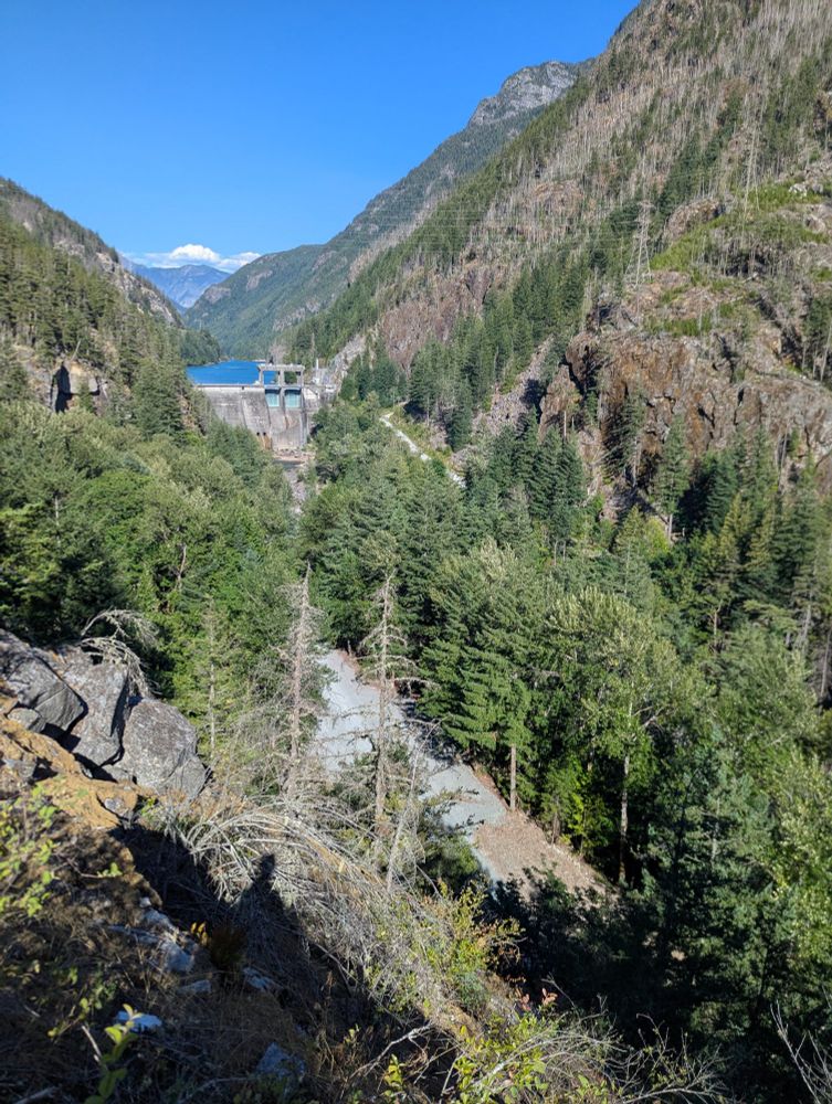 A dam in a narrow canyon with trees and an empty riverbed below