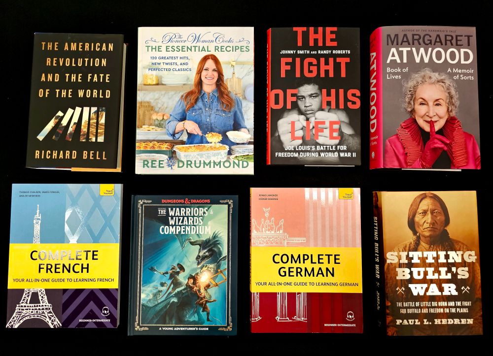 Eight nonfiction books on a table, from top left: The American Revolution and the Fate of the World by Richard Bell, The Pioneer Woman Cooks the Essential Recipes by Ree Drummond, The Fight of His Life by Johnny Smith and Randy Roberts, Book of Lives by Margaret Atwood, Complete French, D&D Warriors & Wizards Compendium for Young Adventurers, Complete German, and Sitting Bull's War by Paul L. Hedren.