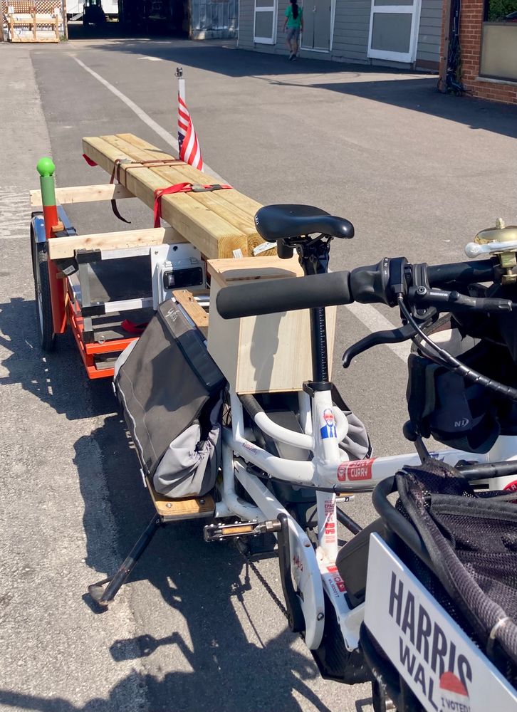 Yuba Spicy Curry cargo bike towing a trailer with 3 8’ 4x4 posts. 