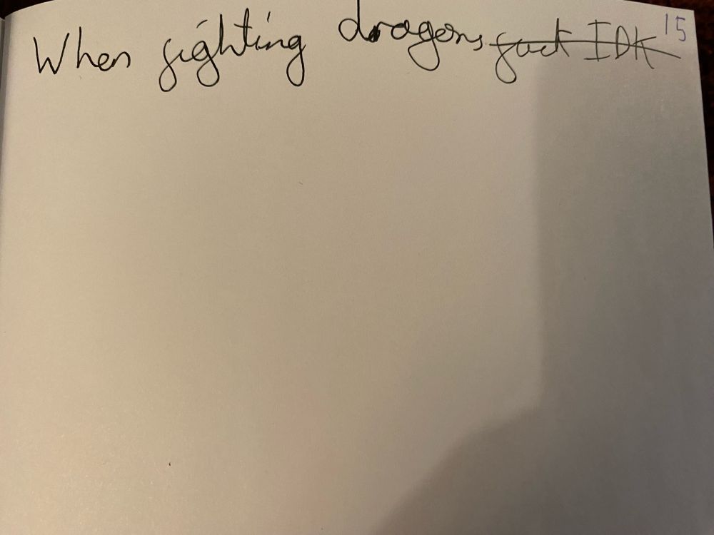 A blank page that has the beginning of a sentence reading ‘when fighting dragons’ handwritten in black ink. Immediately after it the words ‘fuck IDK’ are also written and have been crossed out. The number 15 is also written in the corner in blue ink.