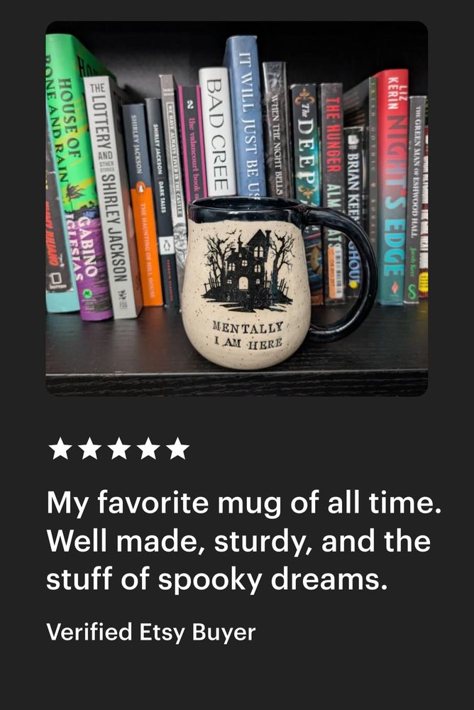 A photo of a handmade pottery mug made from white speckled clay and glazed black on the handle, rim, and interior. It has a black haunted house image on the outside and reads MENTALLY I AM HERE. The mug is resting on a bookshelf full of books. 

Below the photo it reads:
⭐️⭐️⭐️⭐️⭐️
My favorite mug of all time.
Well made, sturdy, and the stuff of spooky dreams.
Verified Etsy Buyer