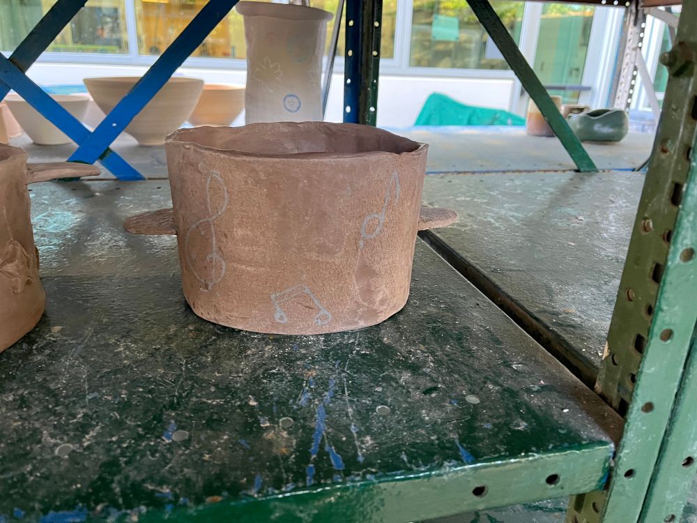 Ceramic large round pot made of brown clay. Pot is decorated with gray (will fire black) music notes, treble clefs, and other various music motifs. The pot has not been fired or glazed.