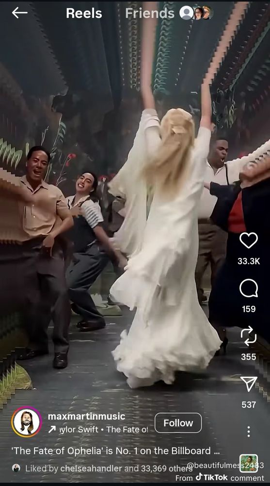 screenshot from Max Martin tiktok of Taylor Swift in white dressed, with her back facing the screen and her arms outstretched he’d upwards. There appears to be a paper or clip of some kind in her hair.