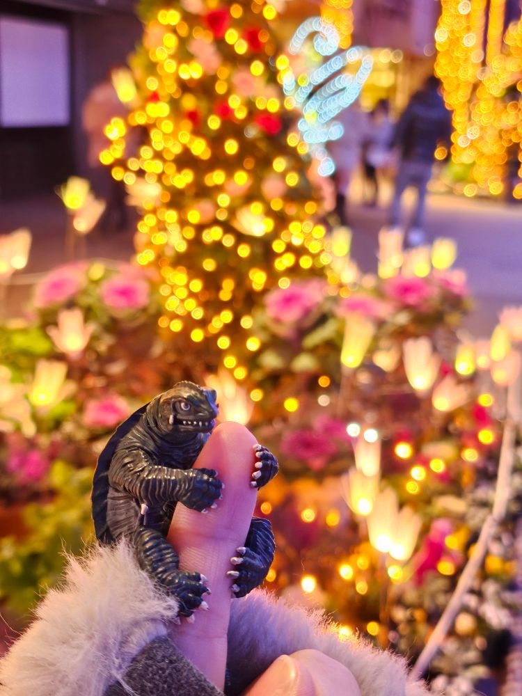[写真]イルミネーションで飾られた花壇の前のガメラのフィギュア。