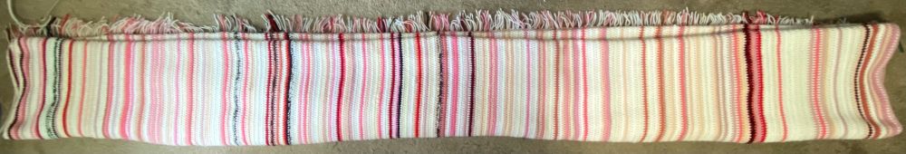 The same crochet blanket folded longways to show all the stripes. The seven new rows on the far right are white, light rose, pale peach, light rose, medium rose, white, and medium rose.