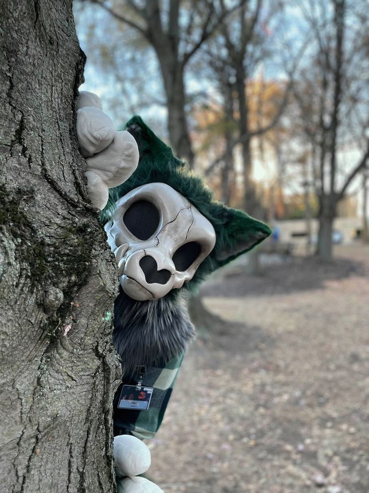 real life picture of a green and bone colored skullbeast fursuit behind a tree