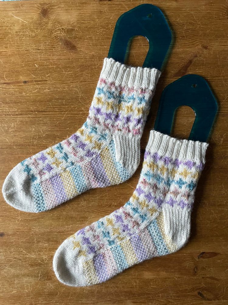 a pair of hand-knit socks with a pattern of four-pointed stars in pastel shades on a cream background.