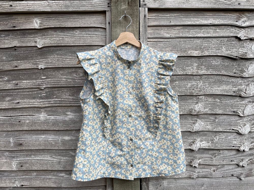 a hand-made sleeveless shirt with ruffles down both sides acting as cap sleeves. the fabric is pale blue with cream flowers. 