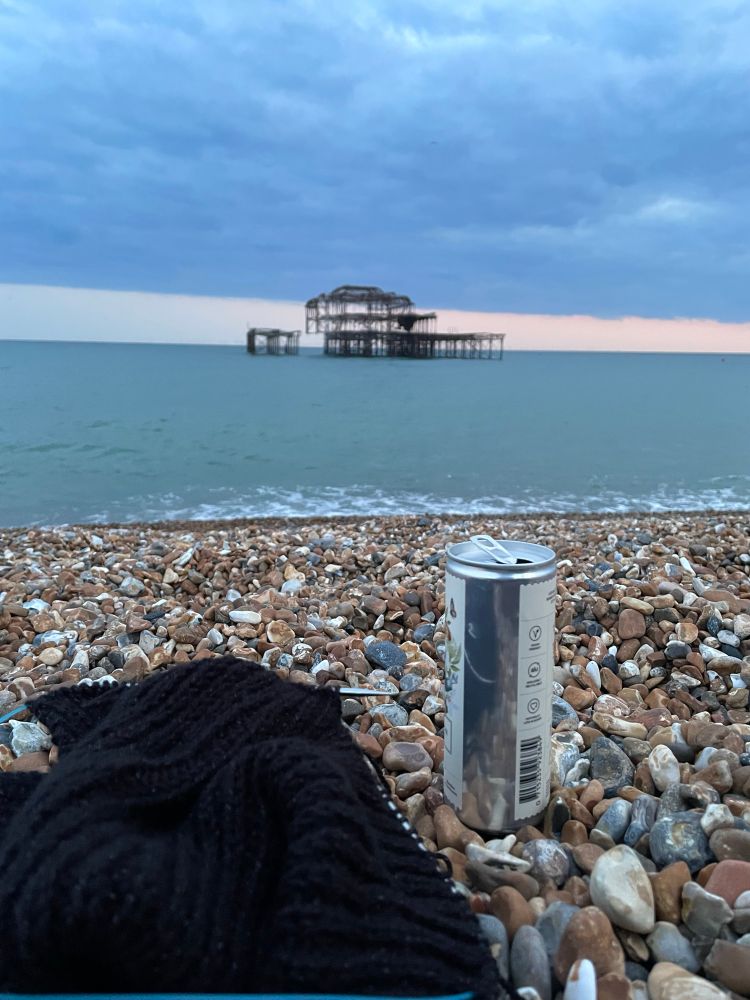 A knitting WIP on a stony beach with the skeleton of Brighton’s old pier in the background