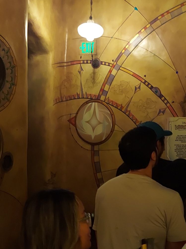 A Lorcana logo taking the place of a Disney character at the entrance to Beast's Library/The Great Illuminary. A sign informs visitors that guest responses will be monitored.