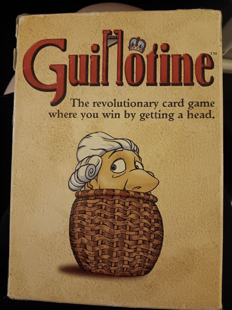 A head in a basket on the front of a box of cards for a game called Guillotine - the revolutionary card game where you win by getting a head