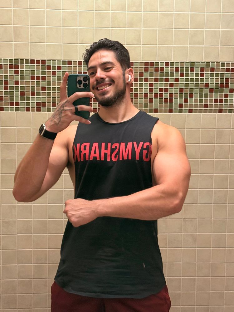 Seismic flexing in a black Gym Shark cut off tank with his arm across his torso