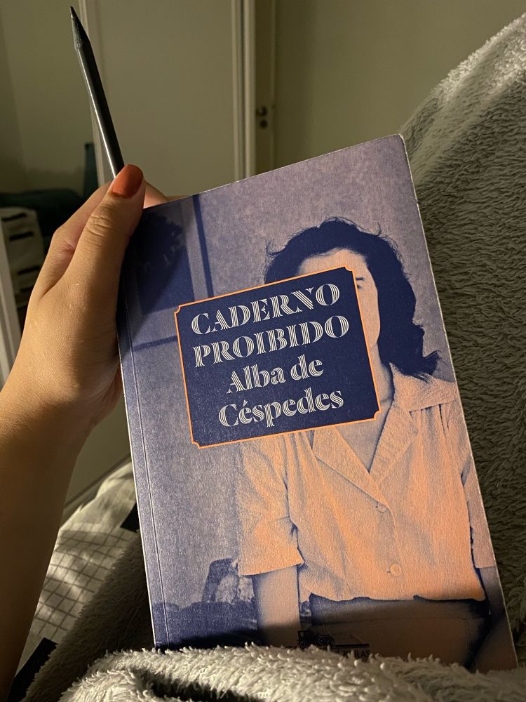 uma mão segurando com iluminação indireta um livro chamado caderno proibido da autora alba de céspedes 
