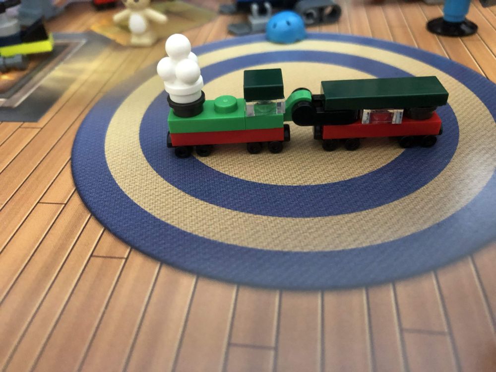 A tiny toy steamtrain, consisting of a locomotive and one passenger carriage. Both have red lower sides, with the loc having a light green top side. The carriage and loc both have dark green roofs and there is a large white smoke cloud coming out of the chimney at the front of the loc. Nifty use of an ice cream piece, i must say!