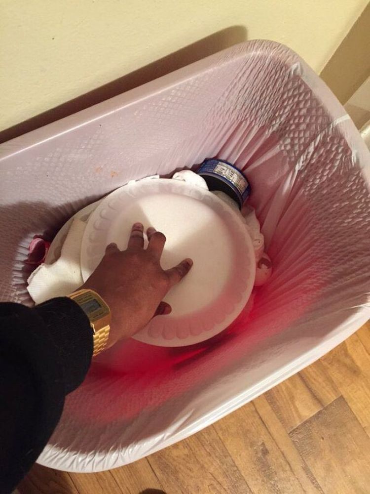 Someone's hand with a gold watch and a black sleeve, putting a plate in the trash upside down