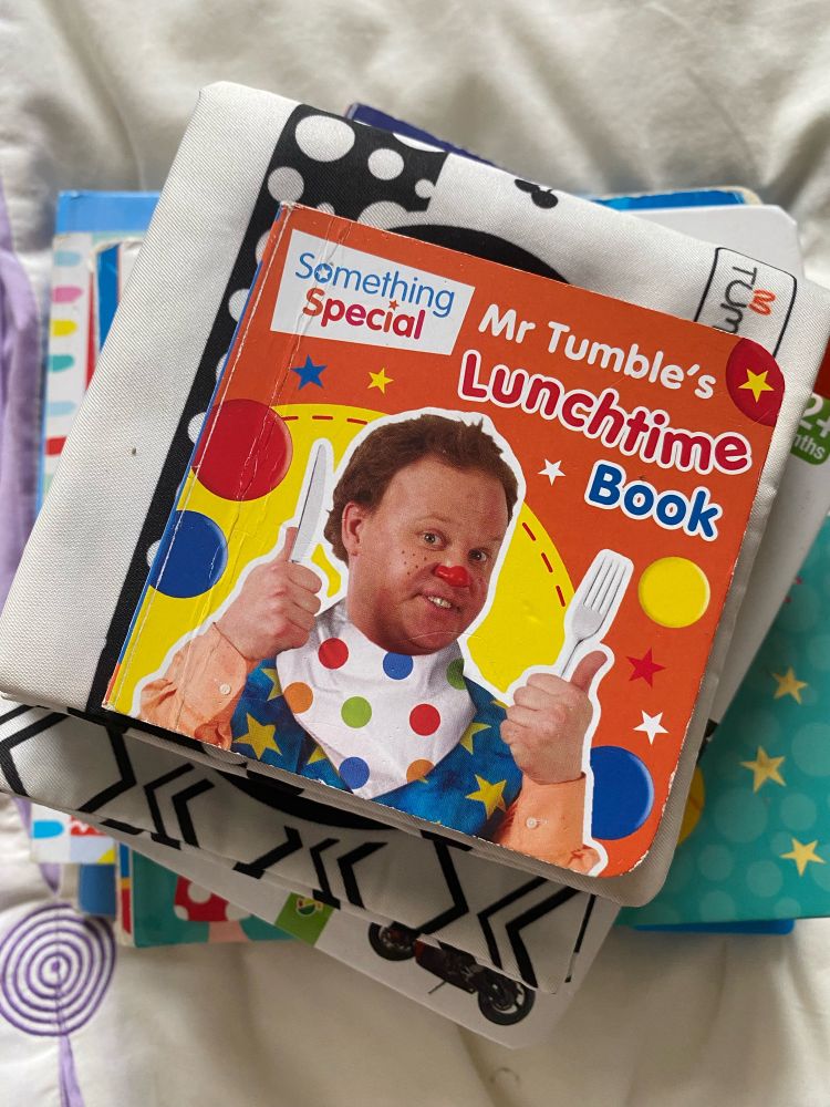 A small children’s book called Something Special: Mr Tumbles Lunchtime Book

It’s orange and yellow, with a picture of a clown with a colourful, spotted bib holding up a knife and fork.
