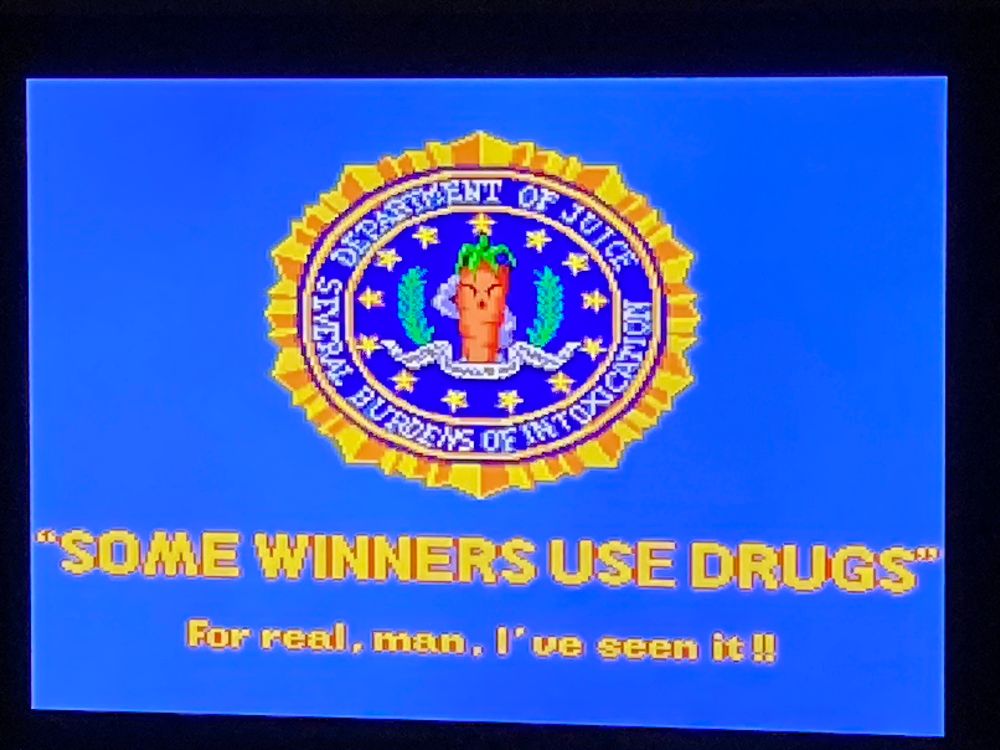 A joke disclaimer from the start screen of Metal Dragon on the Evercade. An official looking seal, similar to that seen on floor of the White House, see here, featuring a carrot saluting the player.The motto surrounding the seal says ‘Department of Juice’ and (separately), ‘Several Burdens of Intoxication’.
Below that, the usual ‘Winners don’t use drugs’ message is replaced with ‘Some Winners Use Drugs, for real man, I’ve seen it!’