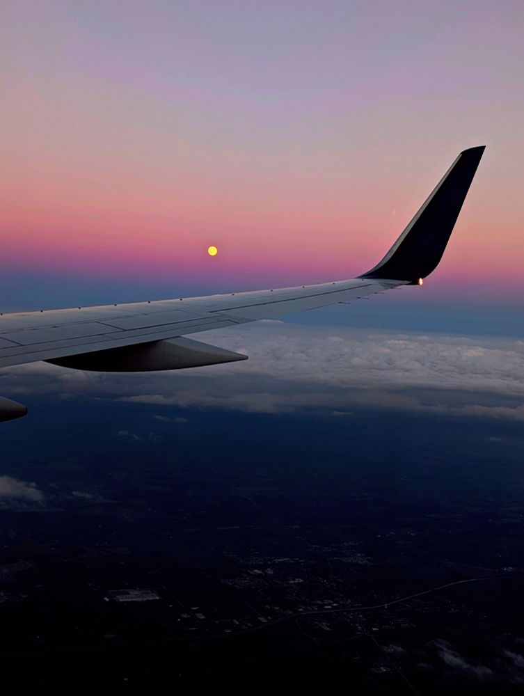 Wing of an Airbus a320 flying over Ohio, an almost-full moon is in the background and a purple/pink sunset 