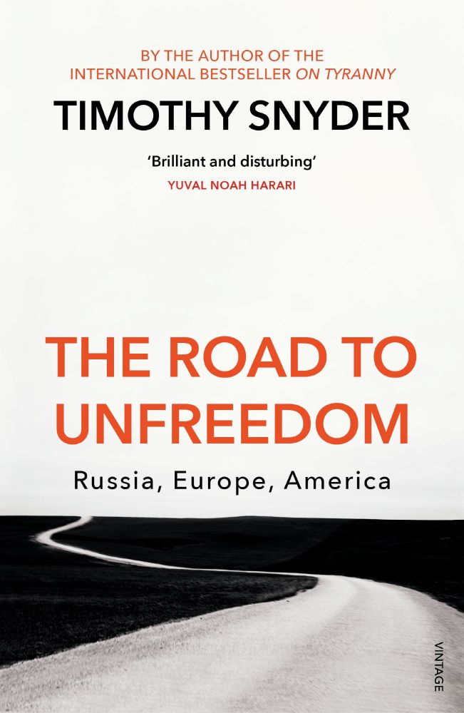 Book cover of The Road to Unfreedom by Timothy Snyder. The design features a black-and-white photograph of a winding road stretching into a barren landscape, symbolizing an uncertain or ominous journey. The title is prominently displayed in bold red-orange letters, with the subtitle “Russia, Europe, America” beneath it. Above the author’s name is a note referencing his previous bestseller On Tyranny, and a quote from Yuval Noah Harari describes the book as “Brilliant and disturbing.” The publisher’s name, “Vintage,” appears vertically in the bottom right corner. 