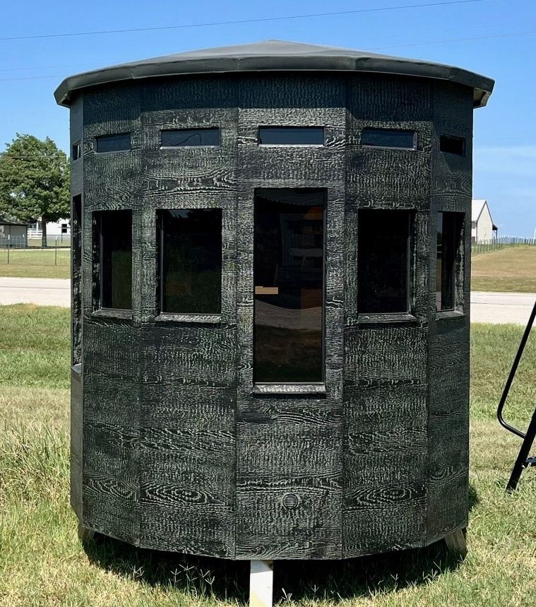 A hunting blind: a small cylindrical shed painted camo green.