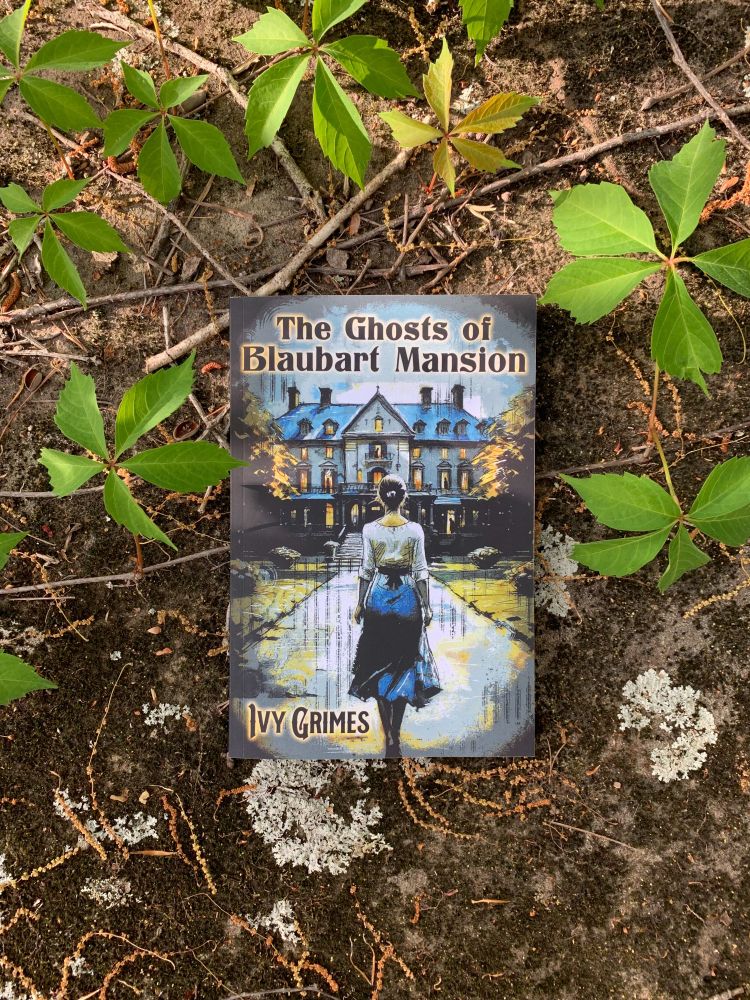 Book on a mossy rock with some green leaves. Book title - The Ghost of Blaubart Mansion. The cover features a young woman approaching an ominious-looking house. 
