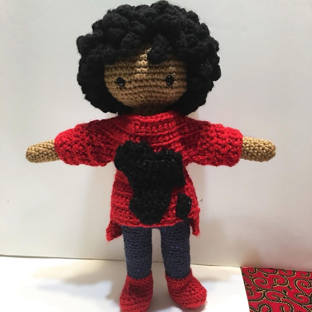 Crochet doll with curly dark hair in red top with black embroidery of Africa blue pants and red boots 