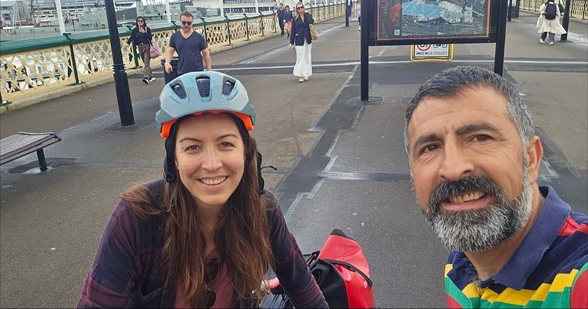A photo of a woman and a man looking into the camera. The woman (me) wearing a bike helmet. In the background is the surface of Pyrmont Bridge