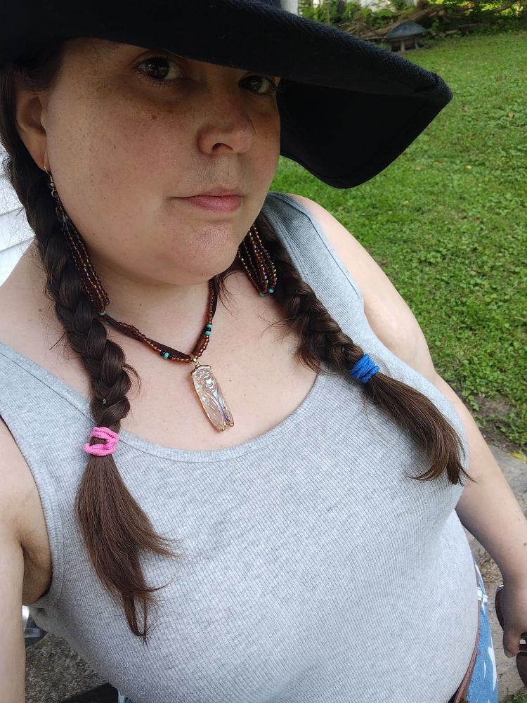 Femme presenting person with braids in her hair, wearing a hat and grey tank top with jeans that have a star pattern on them