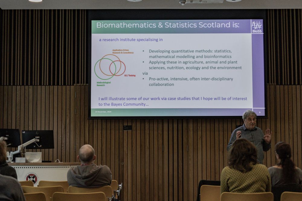 Standing man speaking to the audience in front of a slide describing BioSS work
