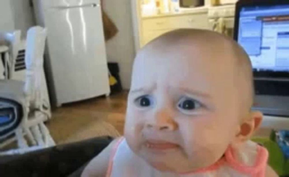 a baby is making a sad face while sitting in front of a laptop .