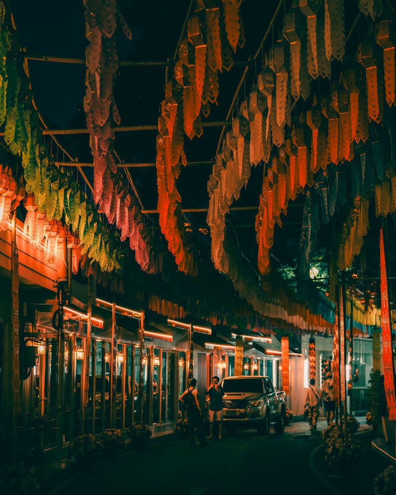 Colorful street in low light with reflections on windows. In the middle is a couple taking pictures behind them is a car. 
