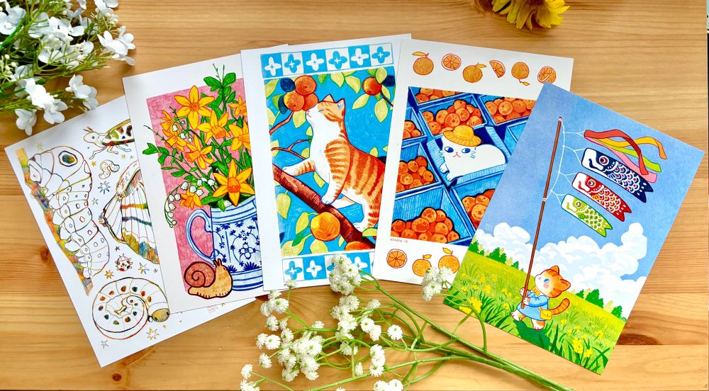 A photo of five different art prints of my illustrations, surrounded by flowers.