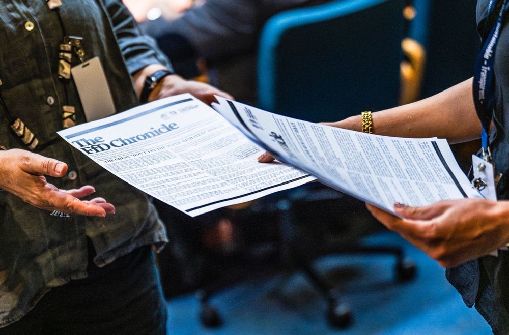 Photo of a person handing a newspaper to someone.