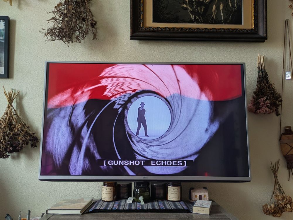 The beginning credits of a James Bond movie, Dr No. The image is of the trademark gunshot part near the end of the credits, as a silhouetted figure dressed in the style of the day stands inside of a white circle, while a black ringed conception of the inside of a pistol frames him. He has shot the viewer, or gun slanger, and the screen is slowly fading to red.
