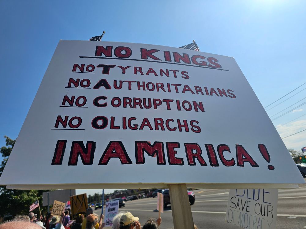 Sign labeled no Kings in America. Included text has No Tyrants, No Authoritarians, No Corruption, No Oligarchs - arranged vertically so that the first letter of each word spelled vertically reads "TACO"