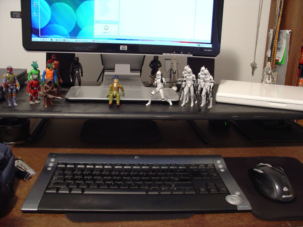 Same as previous but viewing from front/center: Dual-OS computer setup, running Windows on main screen and macOS (back then it was called Mac OS X) on Macbook, with lots of SW action figures in various poses on desk, things hanging on the wall, etc.