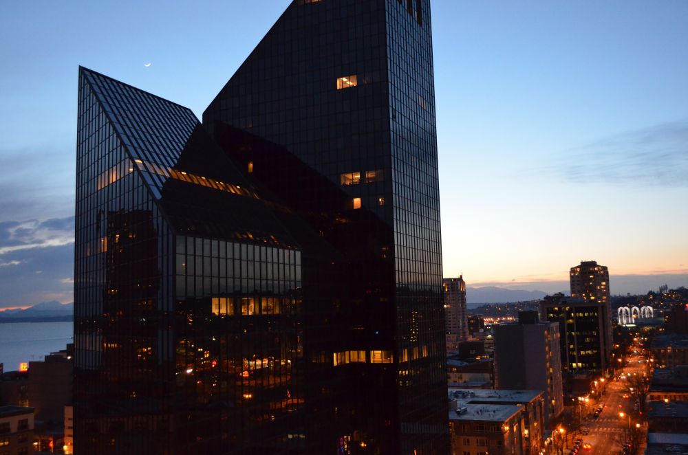 Photo taken near dusk, large geometric building in downtown Seattle, Elliot Bay visible in the distance