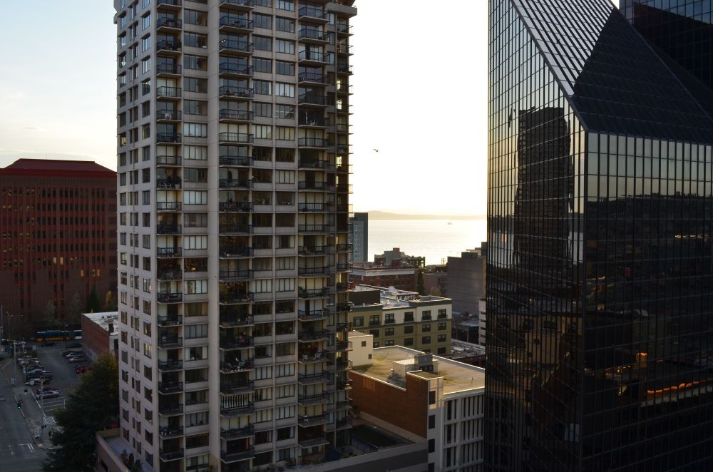 Photo taken near dusk, two large buildings in downtown Seattle, Elliot Bay visible in the distance