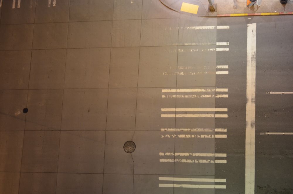 Photo, looking down from hotel balcony, showing street surface with painted crosswalk lines repeating vertically in visually abstract pattern