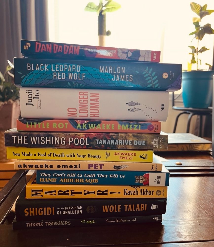 a pile of books sitting on a wood table.

in order:

Dan Da Dan Vol. 6, by Yukinobu Tatsu

Black Leopard Red Wolf, by Marlon James

No Longer Human, by Junji Ito

Little Rot, by Akwaeke Emezi
The Wishing Pool, by Tananarive Due

You Made a Fool of Death with Your Beauty, by Akwaeke Emezi

Pet, by Akwaeke Emezi

They Can’t Kill Us Until They Kill Us, by Hanif Abdurraqib

Martyr! by Kaveh Akbar

Shigidi and the Brass Head of Obalufon, by Wole Talabi

Thyme Travelers, edited by Sonia Sulaiman