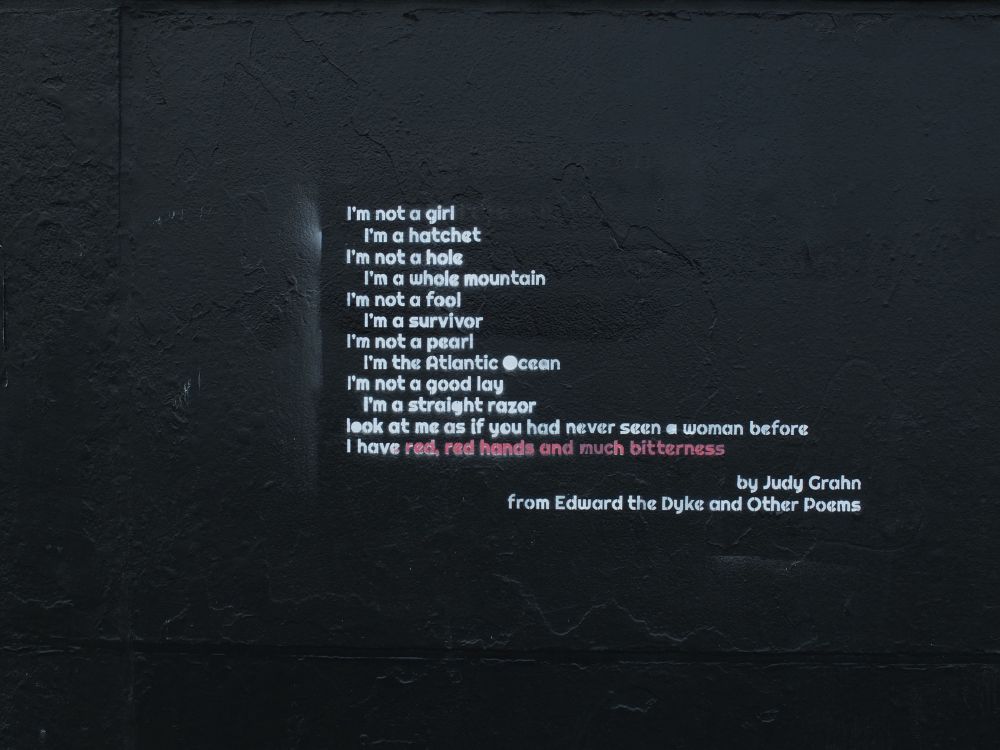 A poem by Judy Grahn painted on a black wall